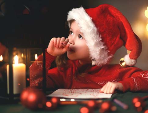 Photo of child with Santa hat writing a letter to Santa.