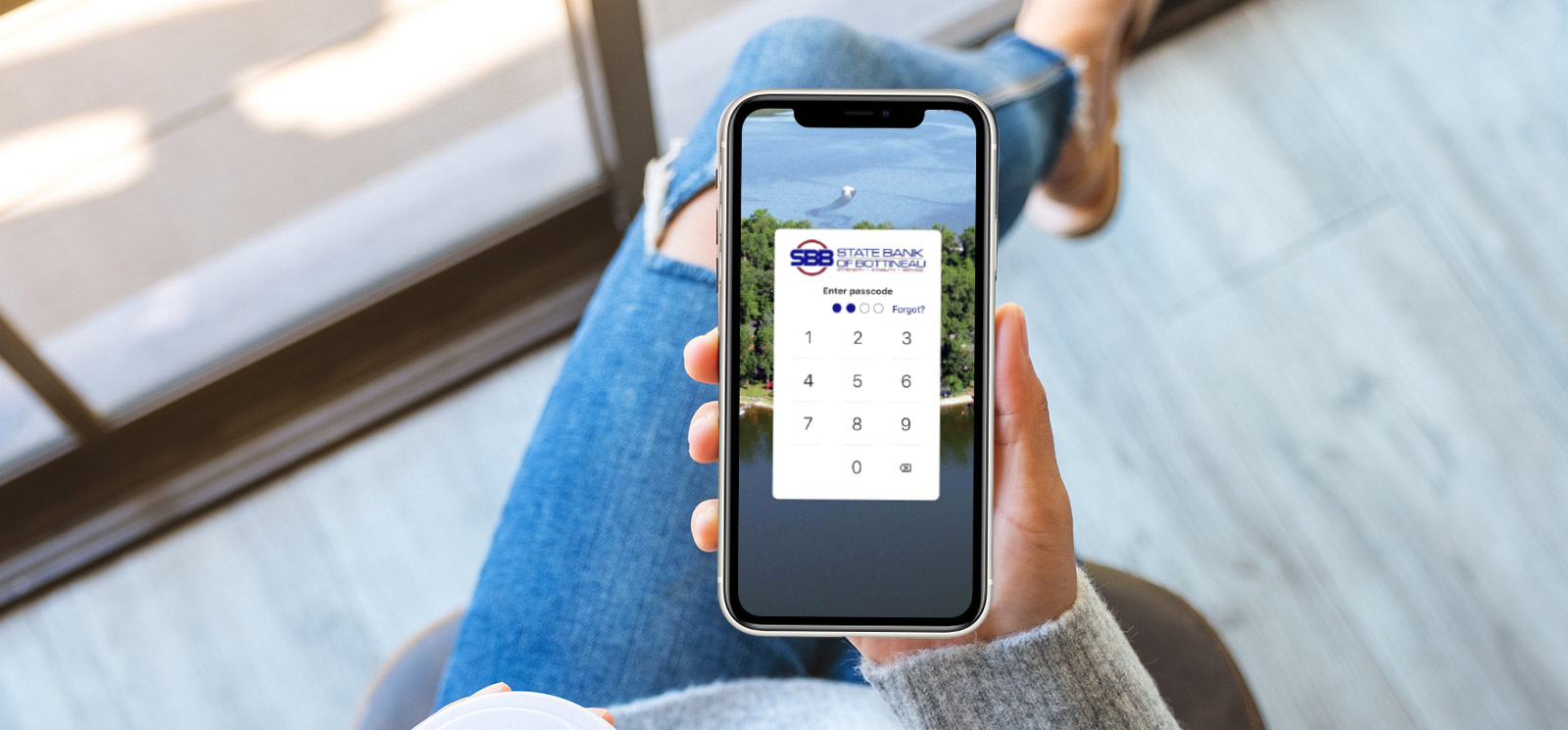 Woman holding phone showing State Bank of Bottineau login screen.